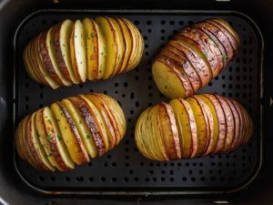 Placing seasoned Hasselback potatoes in air fryer basket